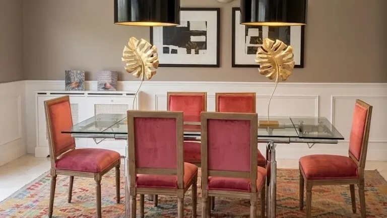 Decoración de comedor elegante con sillas de terciopelo rosa, mesa de cristal y lámparas de diseño con detalles de hojas doradas.