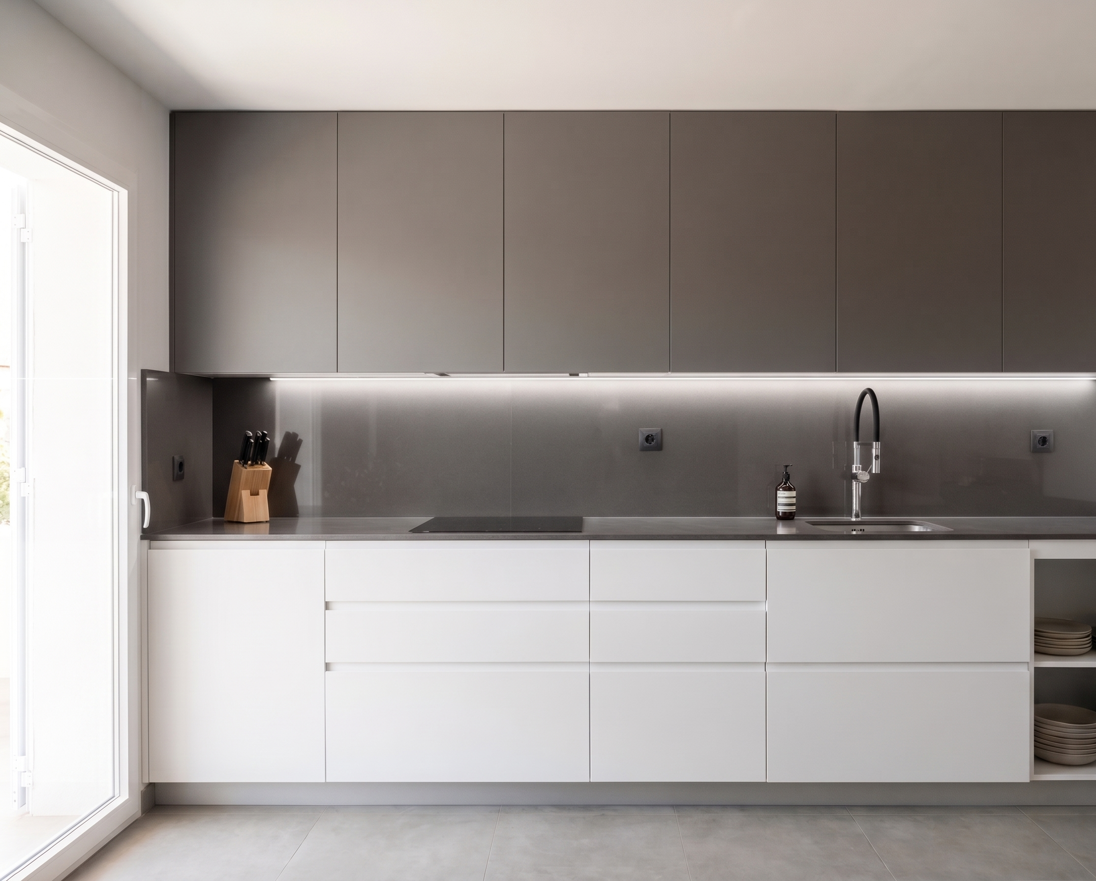 Diseño de renovación de cocina moderna con muebles minimalistas en color blanco y gris, encimera oscura e iluminación LED bajo armario.