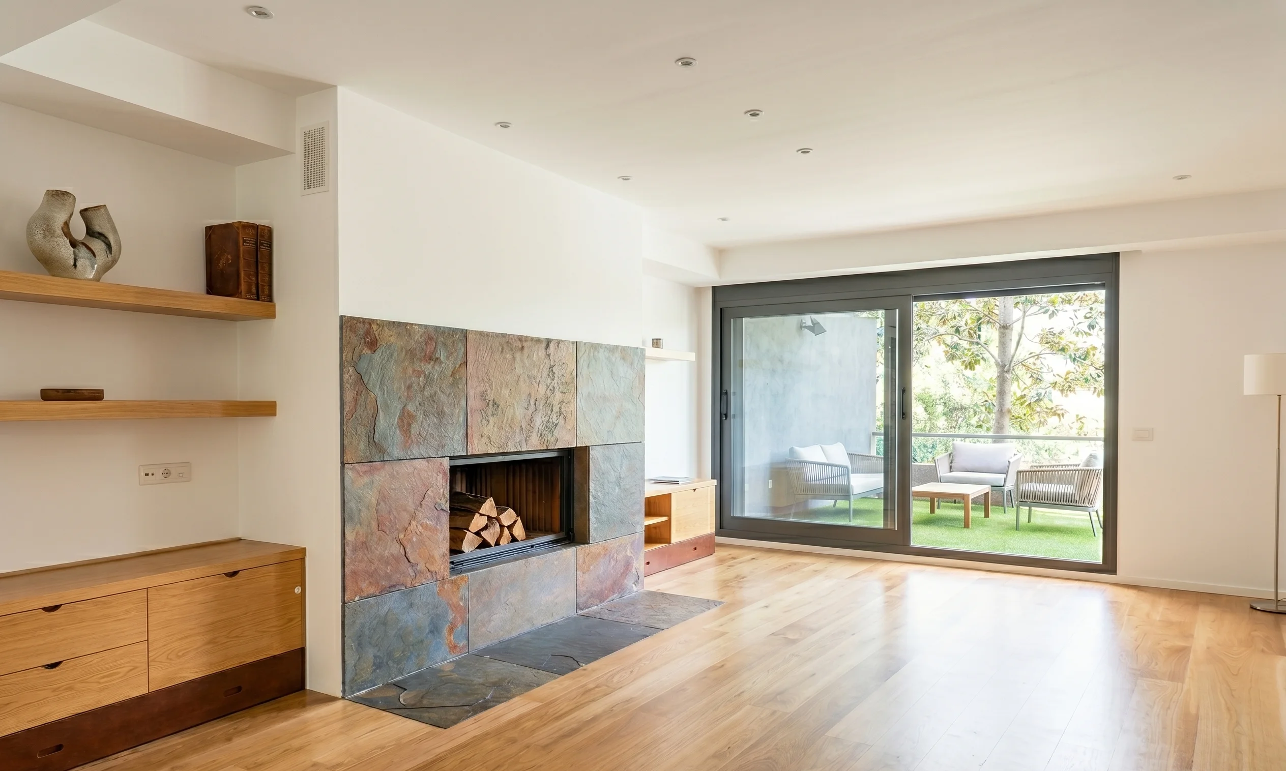 Reforma integral de salón moderno con chimenea de piedra natural, suelo de parquet y salida a terraza